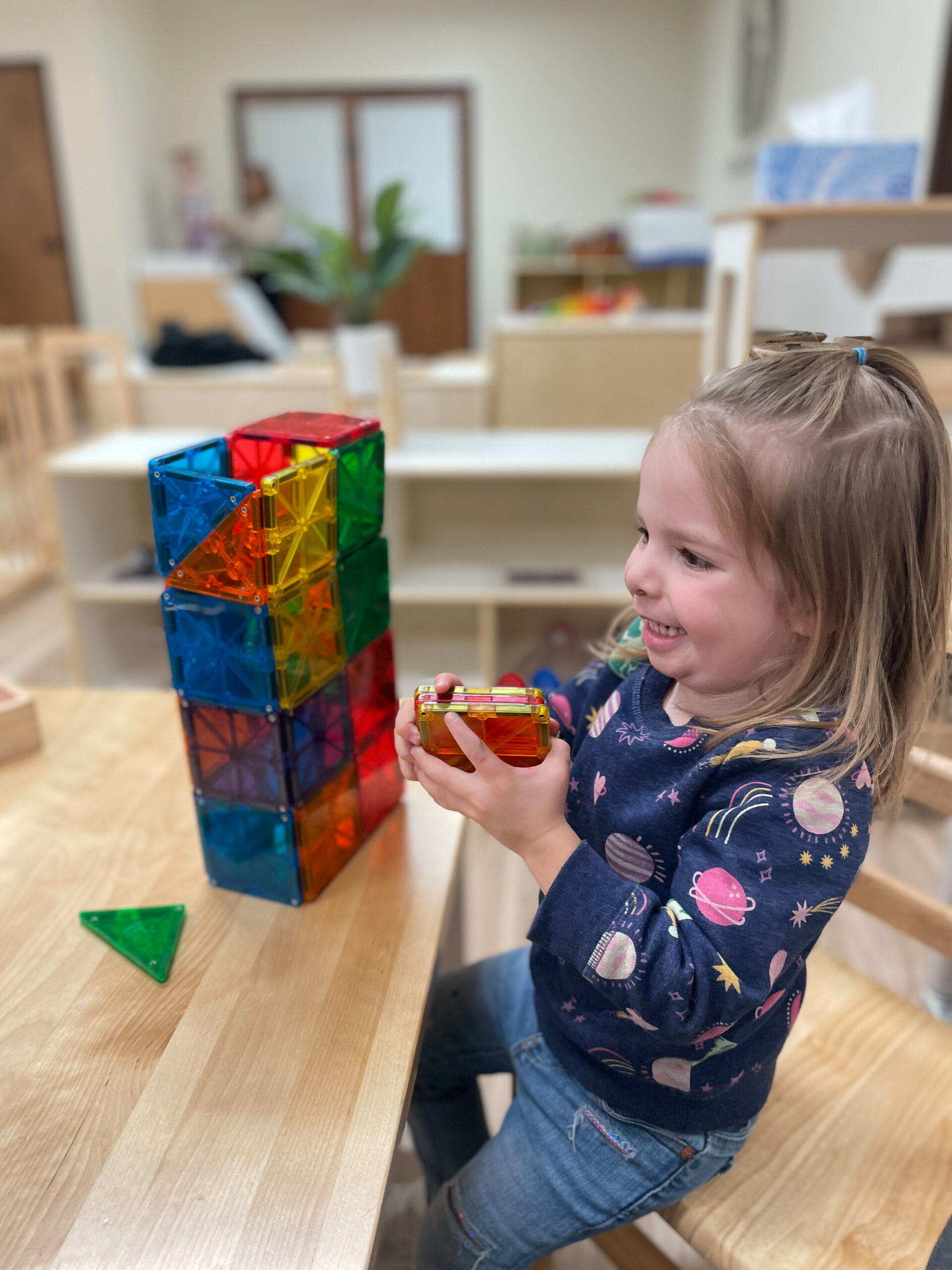 Aviva is hard at work building a tower with magnet tiles at her child care center.