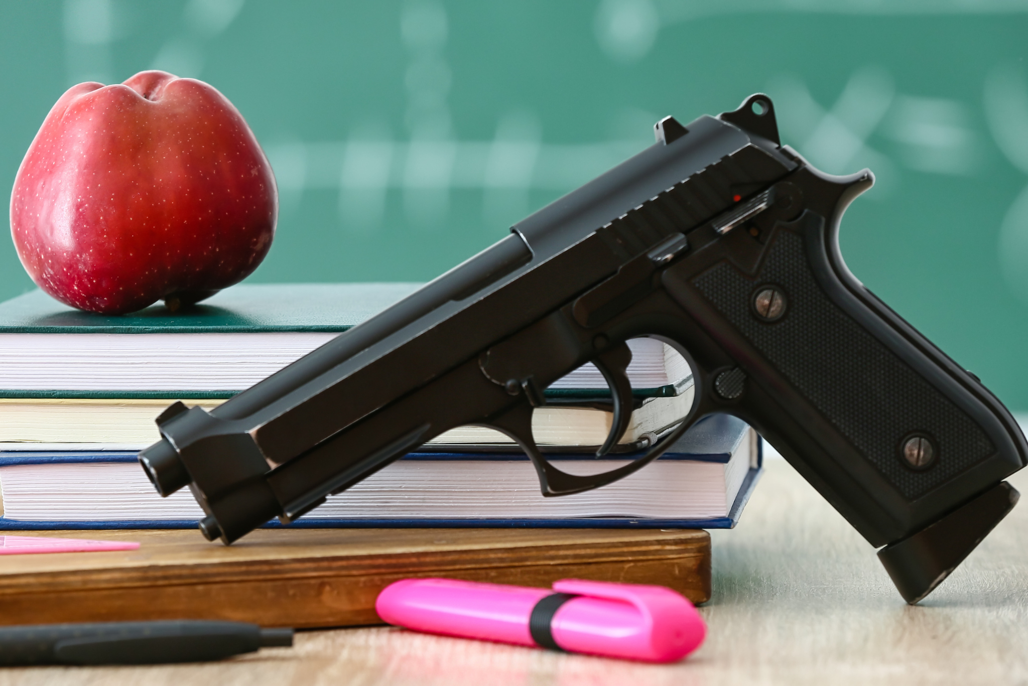 table with an apple, pens, books, and a gun