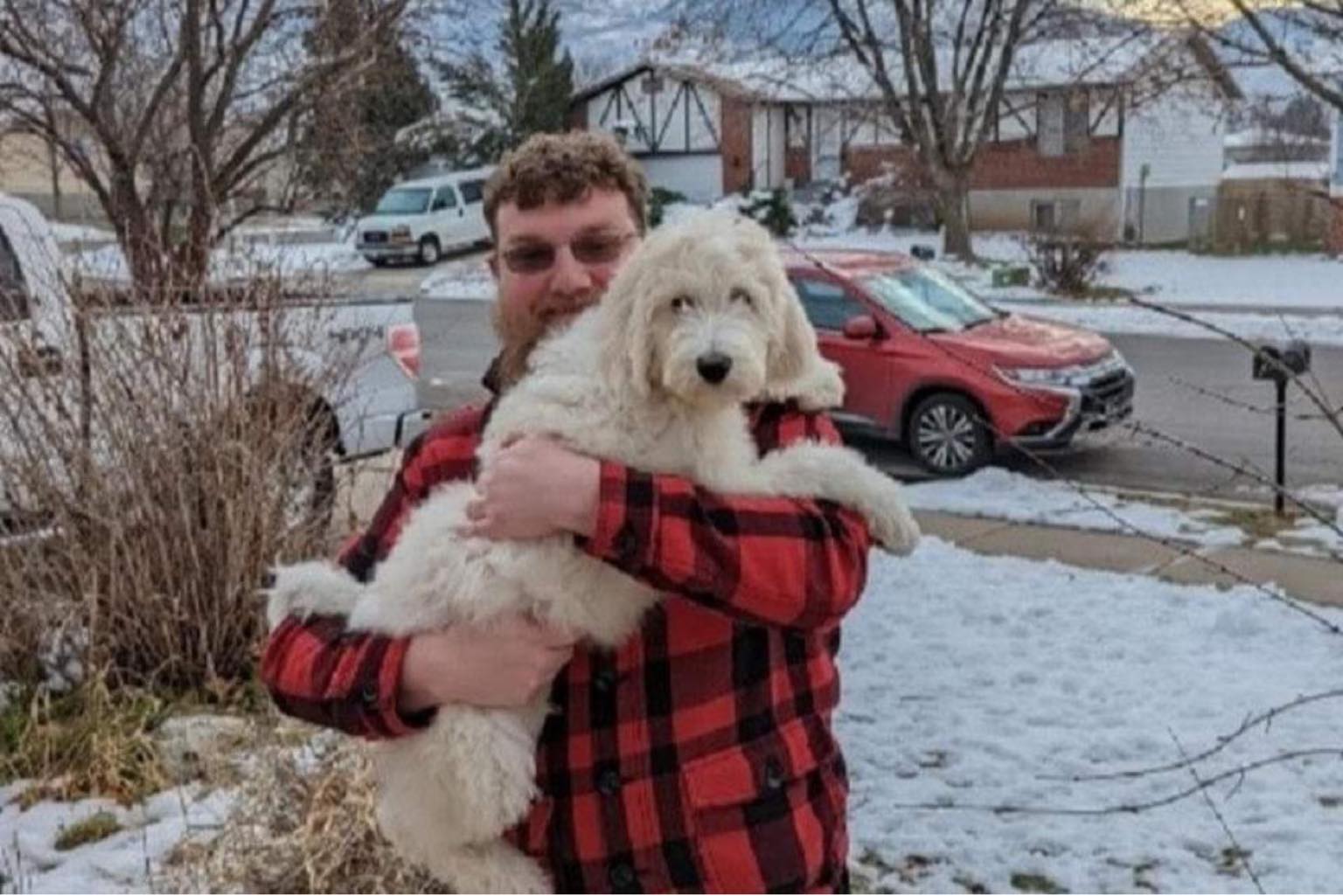 man holding white puppy in snowy front yard