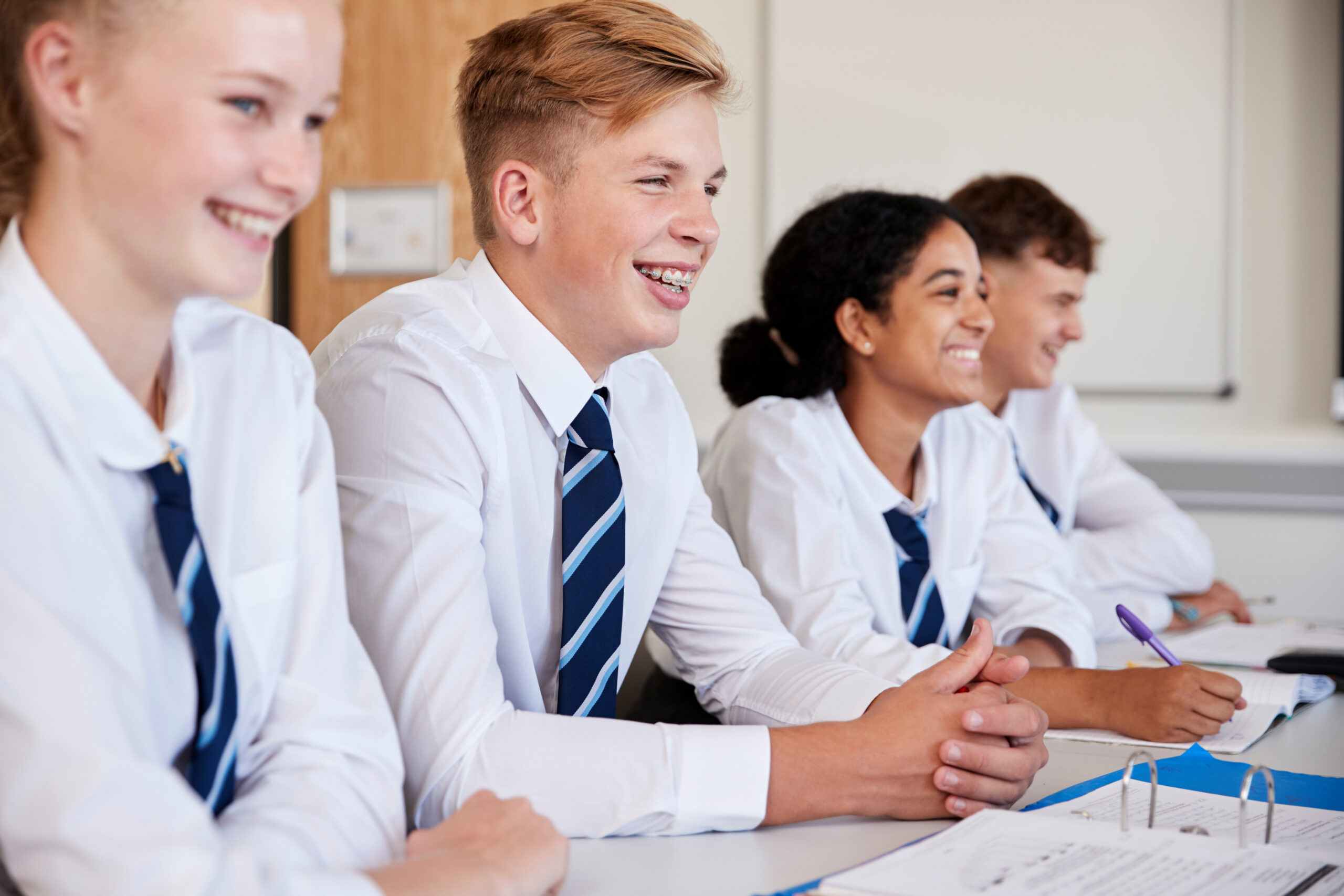 Line Of High School Students Wearing Uniform Sitting At Desk In Classroom